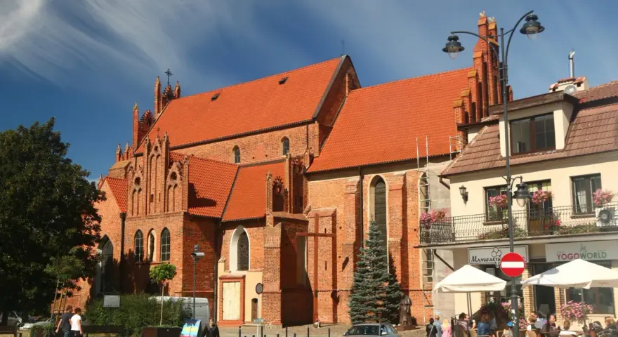 Gotycka ceglana bazylika w Tczewie, z pomarańczowym dachem, to jedna z głównych atrakcji miasta. W tle kawiarniany ogródek.