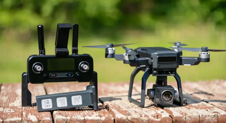 A drone with a 4K camera sits on a wooden table next to its controller and a spare battery, ready for its next follow drone adventure.