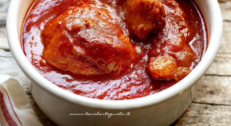 Un saporito ragù napoletano in una ciotola bianca, con pezzi di carne succulenta immersi nel sugo rosso intenso.