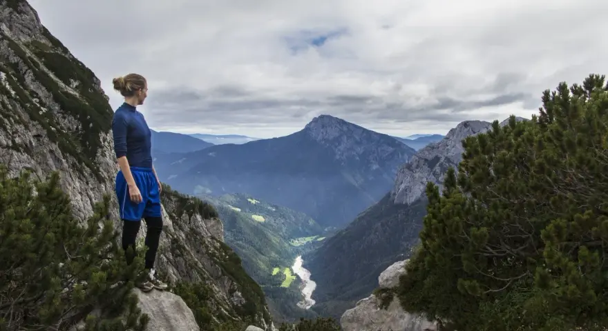 Donna in cima a una montagna, contemplando un vasto paesaggio alpino. Il vero hiking significato è nella libertà e nella vista mozzafiato.