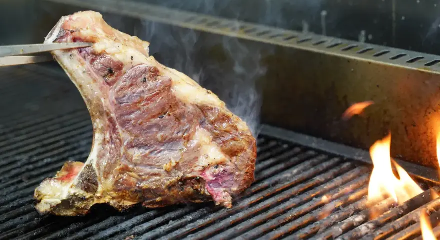 Una succulenta bistecca alla fiorentina, con la sua storia di sapori, cuoce sulla griglia tra fiamme vive e fumo.