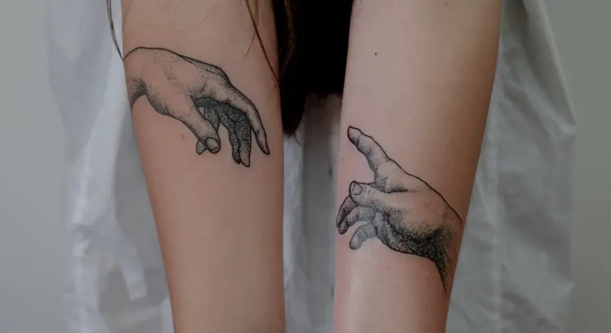 Dwa tatuaże dłoni, jakby sięgały ku sobie, symbolizujące ochronę przed złem i połączenie.