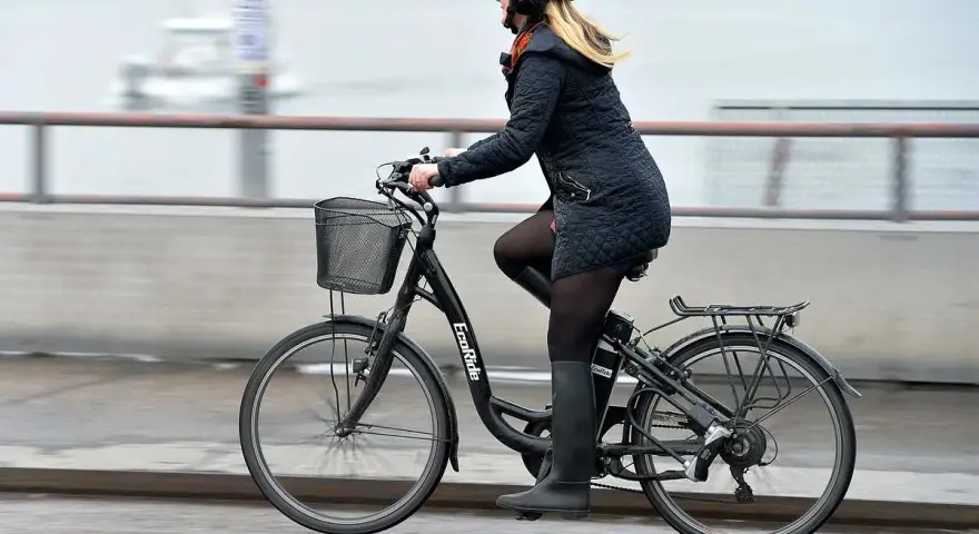 Kvinna cyklar på en elcykel, kanske med bidrag för att underlätta pendlingen. Hon bär hjälm och en varm jacka.