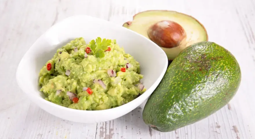 Miseczka guacamole z awokado, cebulą i papryczką chili na drewnianym tle.