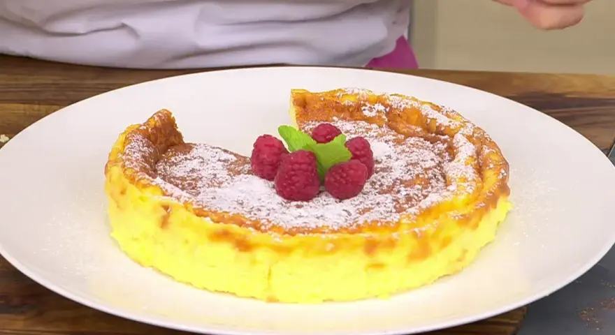 Tarta de queso Arguiñano recién horneada, espolvoreada con azúcar glas y decorada con frambuesas y menta.