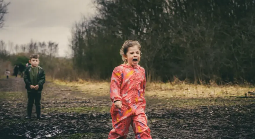Ein 4-jähriges Kind schreit hysterisch in einem Matschfeld. Ein Junge steht im Hintergrund.
