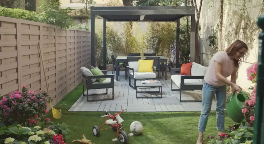 Donna annaffia fiori in un giardino con mobili moderni e un triciclo, un esempio di giardino idee originali.