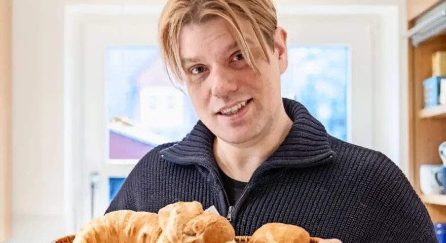Mann mit blonden Haaren hält einen Korb mit frischen Backwaren, darunter ein Croissant und ein Kieler Semmel.