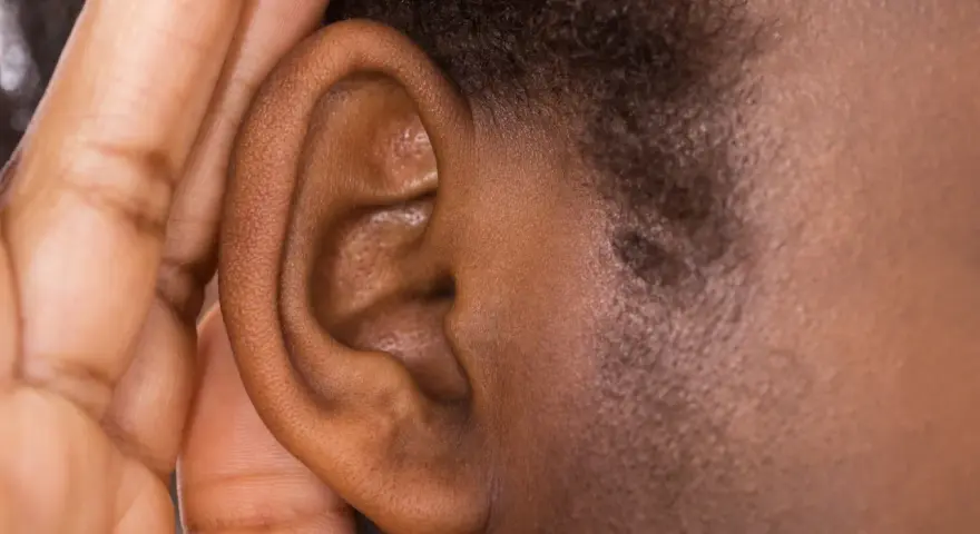 Une main couvre une oreille, comme pour mieux entendre ou se protéger du bruit. Cela peut évoquer ce qu'est-ce qui provoque des acouphènes.