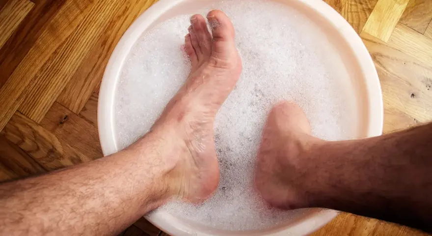 A person's feet soaking in a bubbly foot bath on a wooden floor.