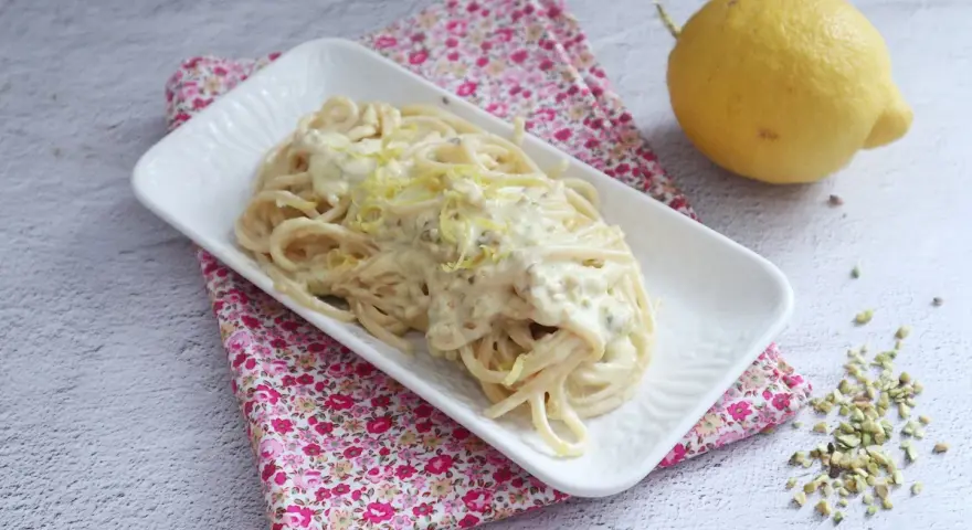 Spaghetti al limone cremosi, un piatto invitante con scorza di limone grattugiata e pistacchi tritati.