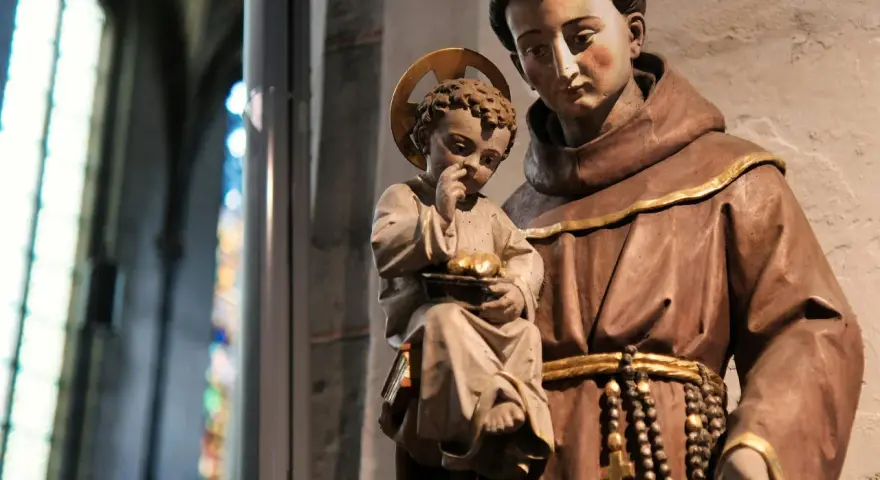 A statue shows what friars wear: brown robes, a cord belt, and a rosary. A child with a halo holds fruit.