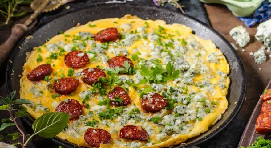 Pyszny omlet na słono z kawałkami chorizo i niebieskim serem, posypany szczypiorkiem i natką pietruszki.
