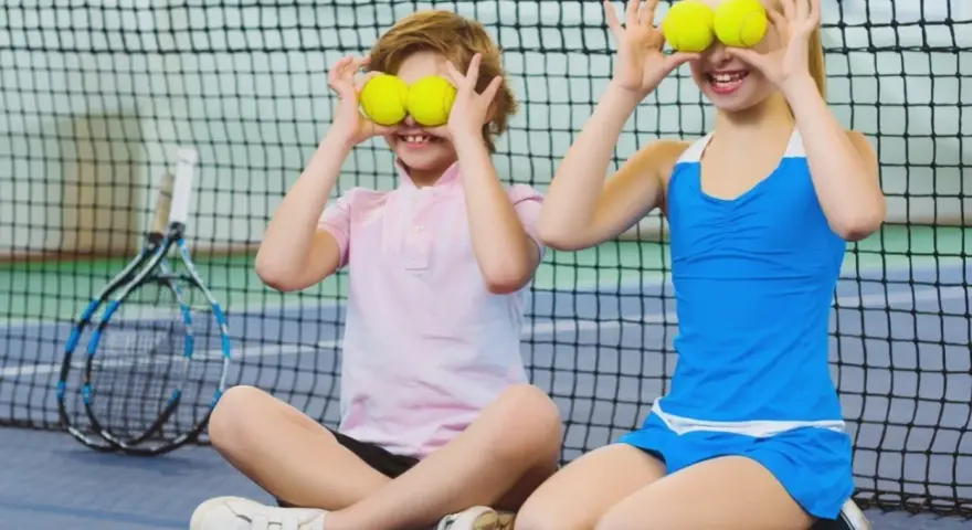 Bambini che fanno sport, con palline da tennis sugli occhi, ridono su un campo da tennis.