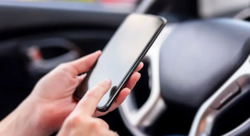 Ręce trzymają smartfon w samochodzie, obok kierownicy. Może to być pomocne, by dowiedzieć się, co to aux i jak podłączyć muzykę.