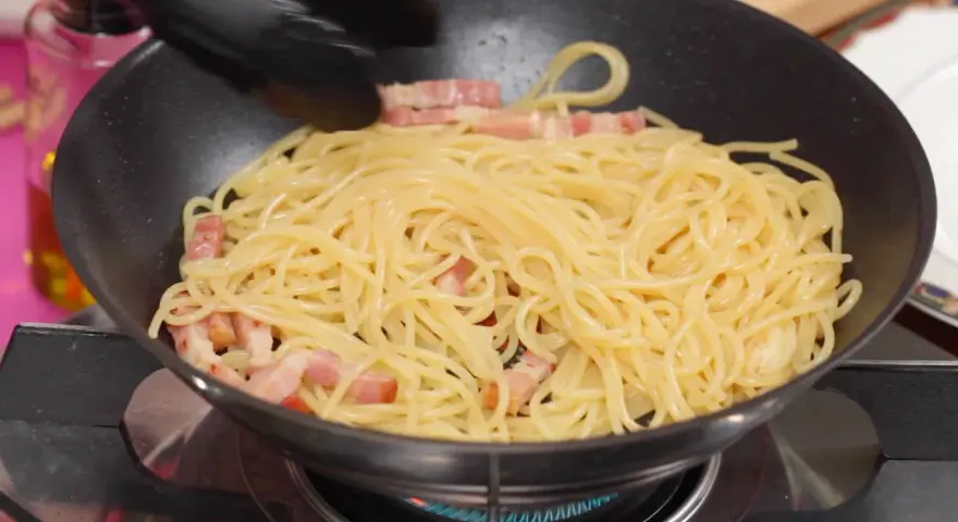 Espaguetis con trozos de panceta en una sartén, preparándose para unos deliciosos tallarines a la carbonara.