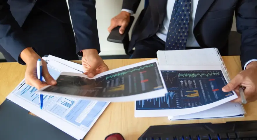 Dos personas analizan gráficos financieros, discutiendo los diferentes tipos de auditorías y sus implicaciones para el negocio.