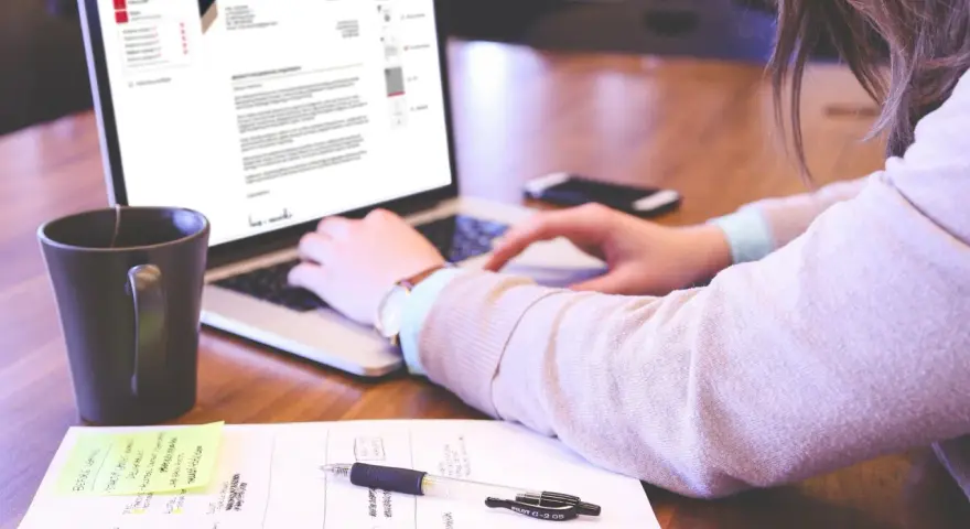 Kobieta pisze list motywacyjny bez doświadczenia na laptopie, obok kubek kawy i notatki.