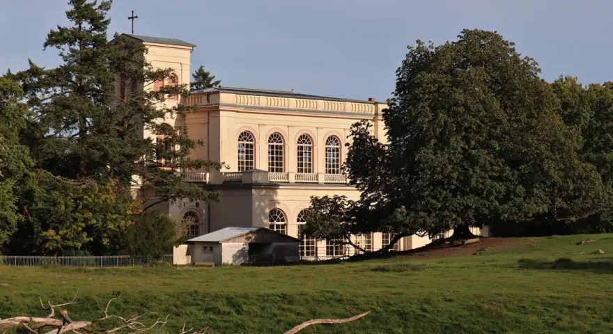 Prachtvolles Gebäude in der **Putbus Altstadt** mit Kirchturm und großen Rundbogenfenstern, umgeben von Bäumen und einer grünen Wiese.