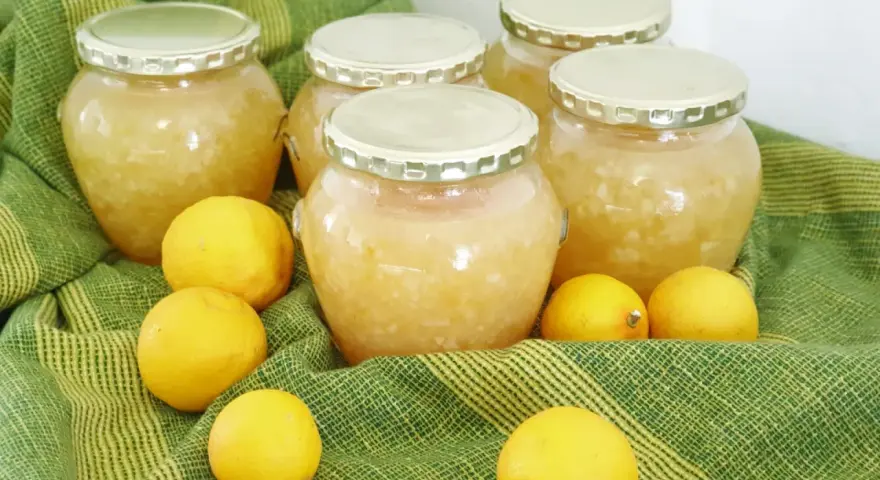 Plusieurs bocaux de confiture de citron maison, entourés de citrons frais, sur un tissu vert rayé.