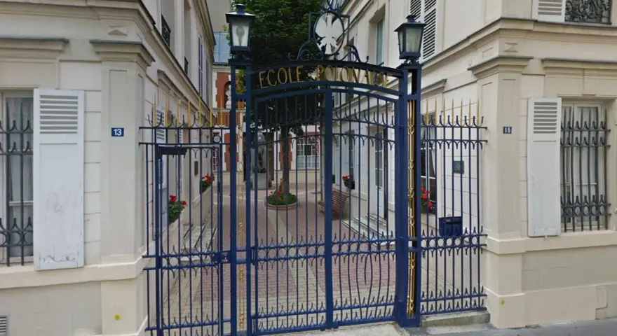 Brama do Ecole de Paris, ozdobiona złotymi detalami, prowadzi na dziedziniec z drzewem i ławką.