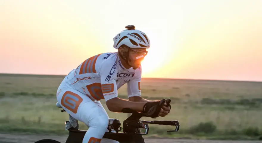 Cyclist in aerodynamic gear races across America at sunset, pushing through the vast landscape.