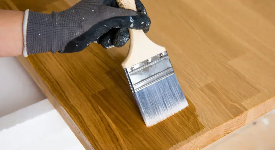 Main tenant avec un pinceau pour enlever l'huile de lin sur du bois.