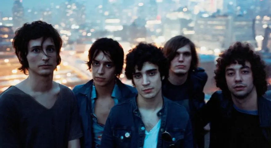 Les membres de The Strokes posent ensemble, le regard tourné vers l'objectif, avec une ville illuminée en arrière-plan.