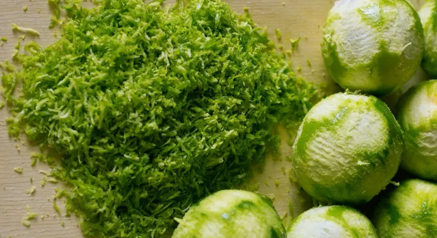 Świeżo starta skórka z limonki, idealna do kordiałów, leży obok kilku obranych owoców.