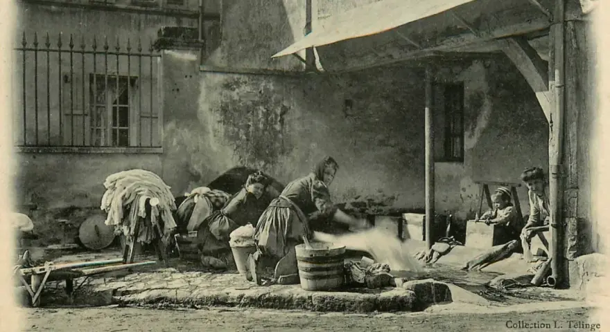 Des femmes s'affairent à laver le linge autrefois, dans une cour. Des enfants observent ce travail pénible.