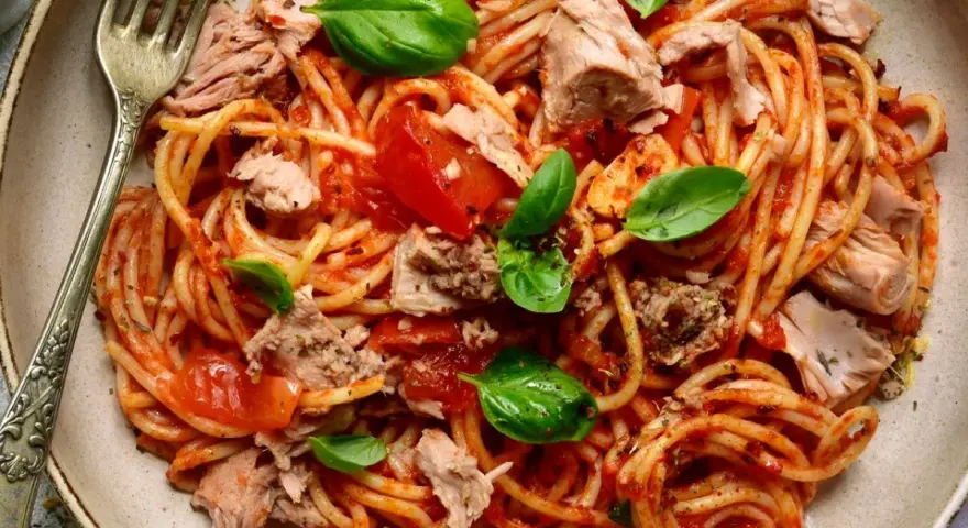 Spaghetti al sugo di pomodoro con abbondante tonno in scatola, guarniti con foglie di basilico fresco. Un piatto semplice e gustoso.