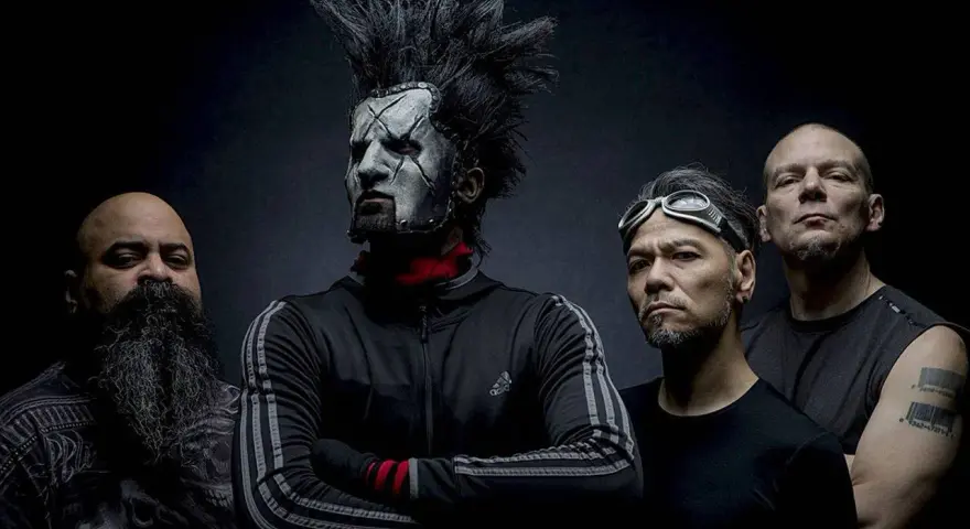 Quatre hommes, dont un avec un maquillage facial blanc et une crête, posent pour une photo. Le groupe Static X semble prêt à monter sur scène.
