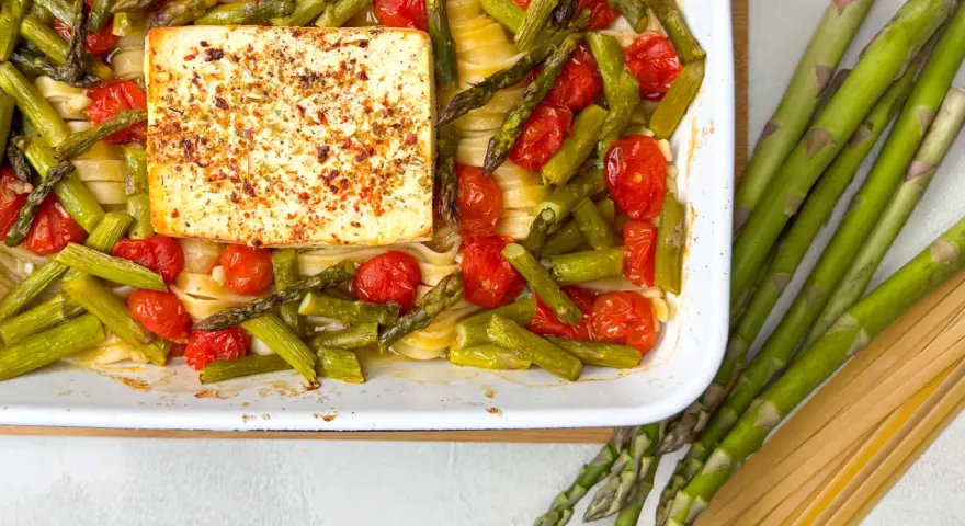 Spargel, Kirschtomaten und Pasta mit einem Block Feta, gewürzt mit Kräutern, in einer Auflaufform.
