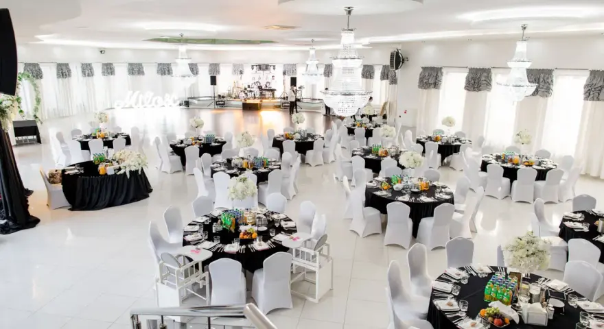 Elegancka sala weselna z czarnymi obrusami i białymi pokrowcami na krzesła. Stoły zastawione, gotowe na przyjęcie gości. Zastanawiasz się, ile za talerzyk na weselu?