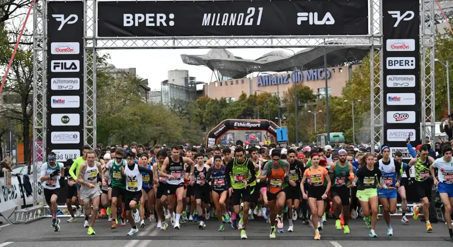 Corredores listos para la media maratón Milán 2021. La carrera arranca bajo un arco con patrocinadores y el logo de Fila.