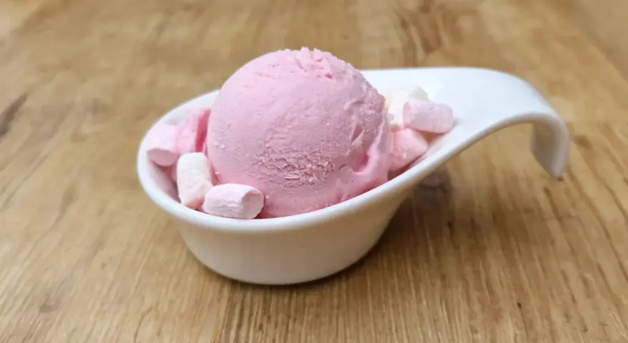 Eine Kugel rosa Bubble Gum Eiscreme mit Marshmallows in einer weißen Schale auf Holzhintergrund.