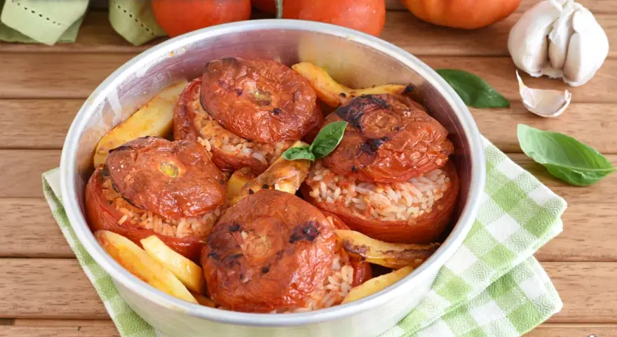 Pomodori ripieni di riso, cotti al forno con patate e basilico. Un piatto estivo saporito e colorato.