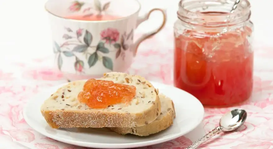 Fetta di pane con marmellata di anguria, tazza da tè fiorita e barattolo di marmellata.