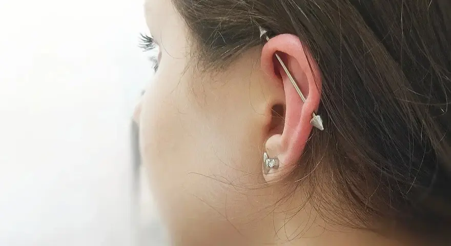 Industrialny piercing ucha z długą sztangą i dwoma stożkami. To przykład, co to jest piercing, który ozdabia ciało.
