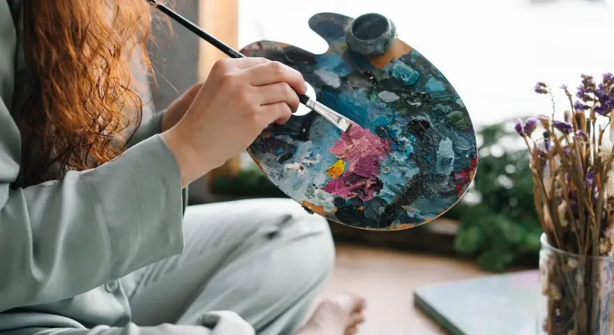 Une artiste aux cheveux roux mélange des couleurs vives sur sa palette, prête à peindre. Apprenez comment utiliser la peinture acrylique pour créer de telles œuvres.