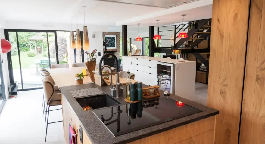 Îlot de cuisine moderne avec plan de travail en granit, évier noir et plaque à induction. La **rénovation cuisine bois massif** se révèle dans les placards et l'îlot central.