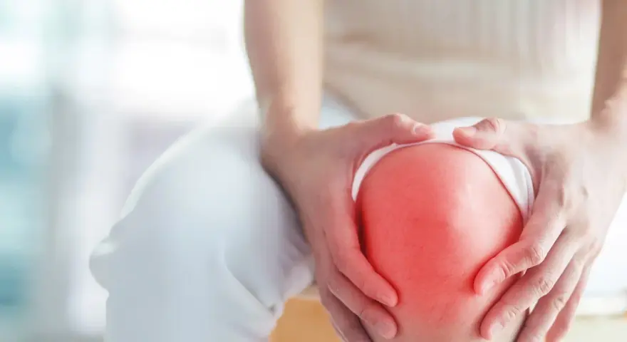 Hände umfassen ein schmerzendes Knie, das rot aufleuchtet, ein Zeichen für Arthrose im Knie.