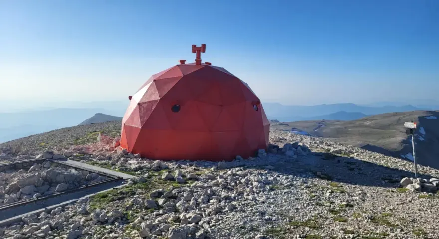 Struttura rossa a cupola su un terreno roccioso, con vista panoramica sulle montagne del Monte Amaro.