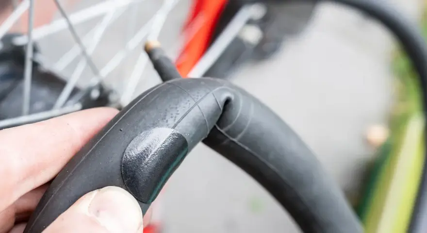 Dłoń trzyma załataną detkę rowerową, gotową do powrotu na swoje miejsce w oponie.