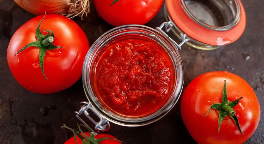 Frische Tomaten um ein Glas mit selbstgemachtem Tomatenmark. Perfekt für Saucen und mehr!