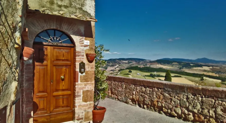 Un portone in legno in un borgo toscano, con vista panoramica sulle colline. Perfetto per un tour in moto tra i borghi più belli della Toscana.