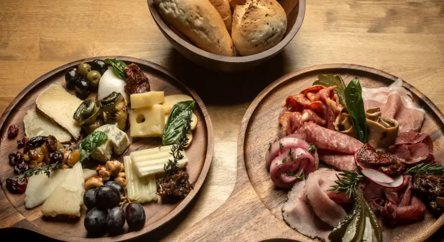 Deska serów i wędlin inspiracje: bogactwo smaków i aromatów na drewnianych deskach, z pieczywem w tle.