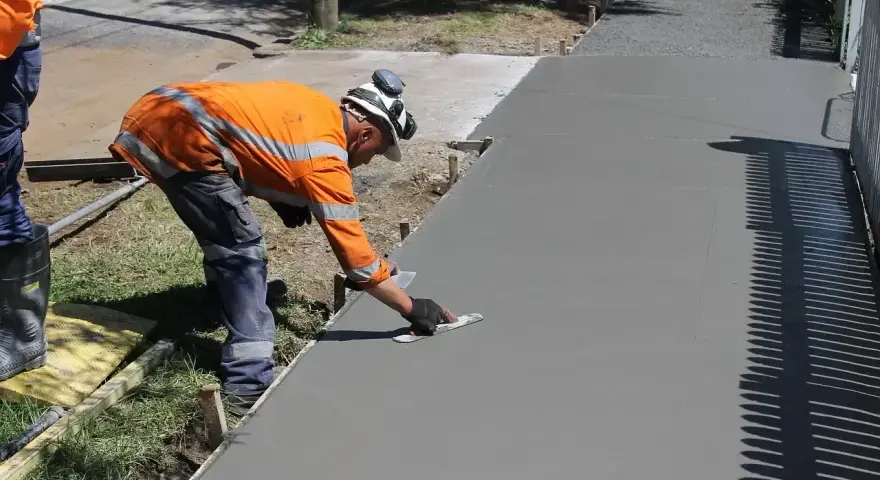 Robotnik w pomarańczowej kamizelce wygładza świeży beton. Zastanawiasz się, ile kosztuje kubik betonu na taki podjazd?