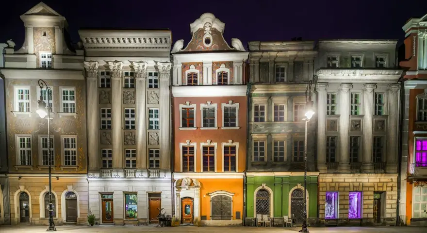 Nocny widok na kolorowe kamienice Starego Rynku w Poznaniu, przypominające urokliwe osiedle warszawskie.