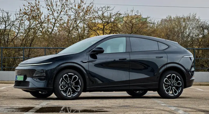 Elegancki, czarny Xpeng G6 stoi na parkingu, odbijając się w kałużach.